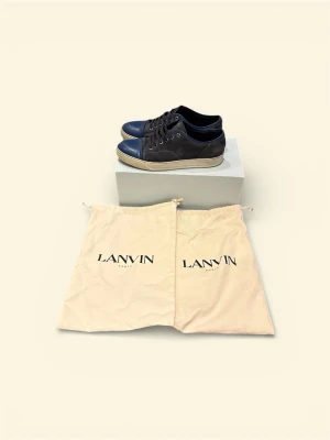 Lanvin cap toe - Snygga mörkblå sneakers från Lanvin med klassisk design. Skorna har rund tå, snörning och vit platt sula. Tillverkade i skinn för en lyxig känsla. Använda vardagligen i ca 6 månader. Ny pris 4499! Säjer då jag har köpt ett par andra skor och har ingen användning av dessa längre! Går att diskutera pris vid snabb och smidig affär!