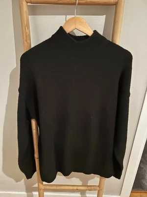 Svart stickad tröja från Bershka - Snygg svart stickad tröja från Bershka med hög hals och avslappnad passform. Tröjan har långa ärmar och ribbade detaljer vid halsen. Perfekt för lager på lager och enkel att matcha med olika outfits.