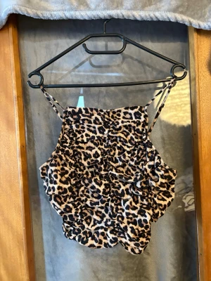 Leopardmönstrad linnetopp med smock - Trendig leopardmönstrad linnetopp med smala justerbara axelband och smockad resår över hela toppen. Toppens material är mjukt och stretchigt, perfekt för att skapa en cool och avslappnad look. Passar perfekt till jeans eller kjol för en snygg outfit.