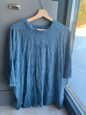 Blå oversized t-shirt från Reclaimed Vintage strl M - Säljer en blå t-shirt från Reclaimed Vintage med broderad text på bröstet. T-shirten har trekvartsärm och är gjord i mjuk bomull. Perfekt för dig som gillar en avslappnad och vintageinspirerad stil.