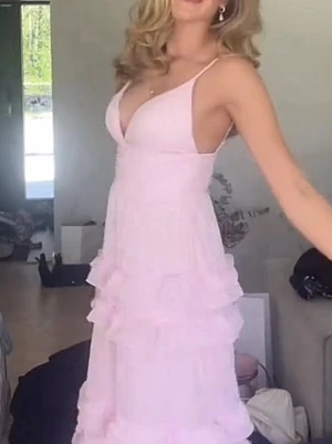 Balklänning - Söt ljusrosa klänning med smala axelband och djup v-ringning. Klänningen har flera lager volanger på kjolen och en feminin, flowy passform. Perfekt för sommarens alla tillfällen men främst skulle jag säga att det är en perfekt balklänning!