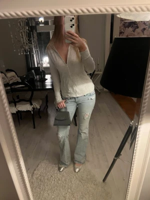 Ljusgrå zip hoodie med v-ringning - Ljusgrå hoodie med dragkedja och djup v-ringning. Tröjan har lång ärm och en relaxed passform. Tillverkad i mjukt material, perfekt för en chill och enkel stil.