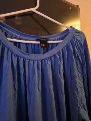 Blå långärmad tröja från Lindex - En blå långärmad tröja från Lindex med rund halsringning och rynkade detaljer upptill. Tröjan är tillverkad i ett mjukt och lätt material, perfekt för lager-på-lager och en avslappnad stil.