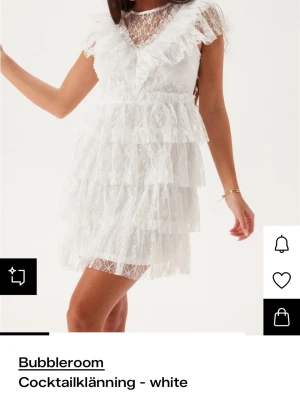Vit spetsklänning från Bubbleroom - Kort vit klänning från Bubbleroom med flera lager volanger och spetsdetaljer. Klänningen har v-ringning, genombruten spets upptill och korta ärmar. Perfekt för dig som vill ha en romantisk och trendig look. Perfekt för student eller skolavslutning