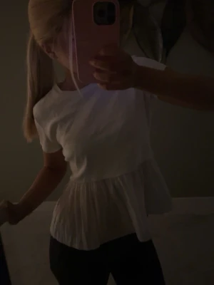 Vit blus med volang - Söt vit blus med korta ärmar och volang nertill. Toppen har en luftig och lätt känsla, perfekt för en fräsch look. Passar till både jeans och kjol för en trendig stil.