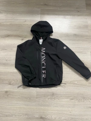 Monclrr vindjacka - Monclrr vindjacka i färgen svart, jackan är i storlek M och är oanvänd och helt ny. Jackan är justerbar runt midjan och runt armarna. Buda gärna!!