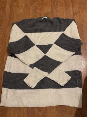 Randig stickad tröja i grått och vitt - Stickad tröja med breda horisontella ränder i grått och vitt. Tröjan har lång ärm och rak passform, perfekt för en avslappnad stil. Mjuk och skön känsla i materialet.