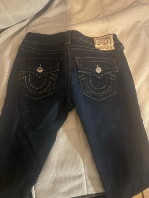 True Religion mörkblå bootcut jeans - Mörkblå jeans från True Religion med ikoniska kontrastsömmar och stora ficklock bak. Bootcut-modell med snygga detaljer på fickorna och silverfärgade knappar. Klassisk jeanslook i kraftig bomullskvalitet.
