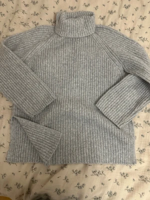 Grå ribbad polotröja stickad - Mysig grå stickad polotröja med ribbad struktur och långa ärmar. Perfekt för kyliga dagar och enkel att styla till olika outfits. Polokragen ger extra värme och en trendig look.