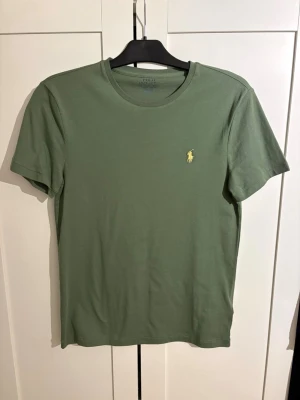 Grön t-shirt från Polo Ralph Lauren - Snygg grön t-shirt från Polo Ralph Lauren med gul broderad logga på bröstet. Modellen är slim fit och har klassisk rund hals och korta ärmar. Perfekt för en stilren och avslappnad look.