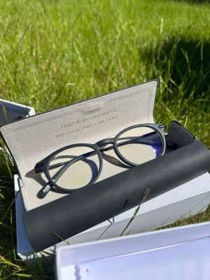 Svarta runda solglasögon AURERA - Snygga svarta antiblåljusglasögon från AURERA med rund form och tunna skalmar. Glasen har en lätt spegeleffekt och bågarna är tillverkade i plast med metallskalm. Perfekta för dig som vill ha en stilren och modern look. Finns ett helt lager så säljer till billigt pris