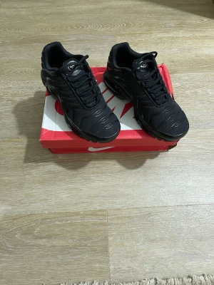 Svarta Nike Air Max sneakers - Säljer ett par svarta Nike Air Max sneakers med klassisk chunky sula och synlig Air-enhet. Skorna har mesh- och syntetpaneler för bra andningsförmåga och komfort. Snygg design med svarta detaljer och snörning. Perfekta för dig som gillar streetwear och sportig stil.