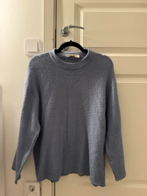 Ljusblå oversized stickad tröja - Mysig ljusblå stickad tröja med avslappnad passform och rund halsringning. Tröjan har långa ärmar och ribbade muddar vid ärmslut och nederkant. Perfekt för lager på lager och chill vardagsstil. Passar för dig som brukar ha storlek S.