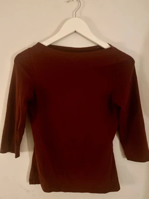 Vinröd topp med 3/4-ärm - En enkel och stilren vinröd topp med 3/4-ärm och rund halsringning. Toppen har en figurnära passform och är tillverkad i mjukt bomullsmaterial. Perfekt att matcha med jeans eller kjol för en clean look.
