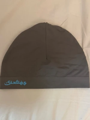 Grå mössa från Sixties - Knappt använd! Snygg grå mössa från Sixties med diskret blå logga framtill. Tillverkad i mjukt och stretchigt material som sitter skönt på huvudet. Enkel design som passar till många olika stilar och outfits.