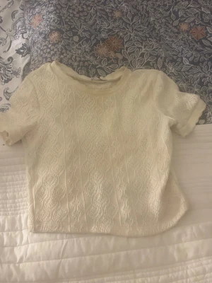 Vit spets topp med kort ärm - Söt vit topp i spets med korta ärmar och rund hals. Croppad modell med fina spetsdetaljer som ger en romantisk känsla. Perfekt att matcha med höga jeans eller kjol.