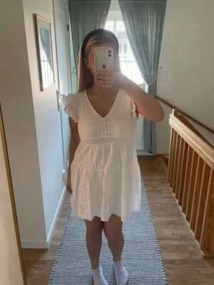 Vit spetsklänning med volangärmar - Söt vit kortklänning med spetsdetaljer och volangärmar. Klänningen har v-ringning och är ärmlös. Perfekt för varma dagar och somriga tillfällen. Bra för student, konfirmation och skolavslutning 