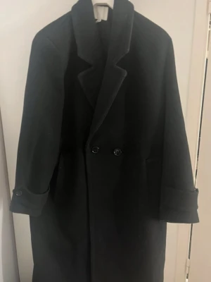 Svart kappa från H&M, storlek M - Säljer en svart kappa från H&M i storlek M. Klassisk modell med dubbelknäppning framtill.