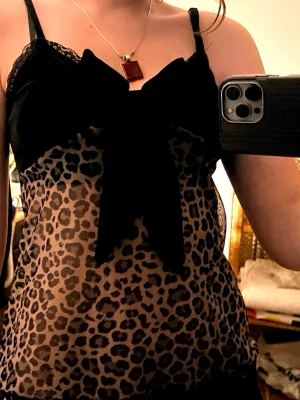 Leopardmönstrad mesh linnetopp från Romwe - Säljer en leopardmönstrad mesh body från Romwe (Shein) med tunna axelband, spetsdetaljer upptill och nedtill och en stor svart rosett framtill. Materialet är genomskinligt mesh i syntet och svart satinliknande (syntet) vid bröstet. Väldigt tunn men perfekt till sommaren eller som nattlinne!💕Aldrig använd 