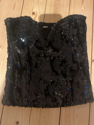 Svart paljett-tubtopp från BikBok - Glittrig svart tubtopp från BikBok täckt med paljetter. Toppen är axelbandslös och har en croppad passform som ger en trendig look. Perfekt för dig som vill sticka ut och glänsa lite extra.