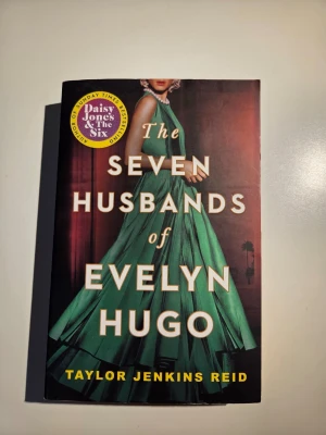 The Seven Husbands of Evelyn Hugo - En engelskspråkig roman av Taylor Jenkins Reid med ett omslag i grönt och guld. Boken handlar om Hollywoodikonen Evelyn Hugo och hennes liv, kärlek och hemligheter. Boken har missfärgade sidor som man kan se på ena bilden men det är inget som syns när man väl läser den. Oklart varför den är missfärgad. 