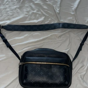 Louis Vuitton svart axelväska monogram - Snygg svart axelväska från Louis Vuitton med klassiskt monogrammönster och justerbar rem. Väskan har en framficka med dragkedja och är tillverkad i skinn med detaljer i silver. Perfekt för dig som vill ha en stilren och lyxig accessoar.