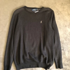 Svart tröja från Polo Ralph Lauren - Svart långärmad tröja från Polo Ralph Lauren i mjuk pima bomull. Klassisk rund halsringning och diskret broderad logga på bröstet. Perfekt för dig som gillar stilrena och tidlösa plagg med premiumkänsla.