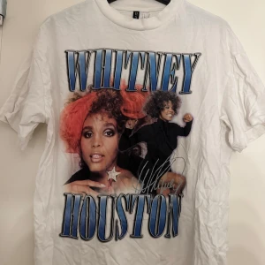 Whitney Houston vit t-shirt med tryck - Säljer en vit t-shirt från H&M med stort Whitney Houston-tryck i blått och svart på framsidan. T-shirten har rund hals och korta ärmar, tillverkad i mjuk bomull. Perfekt för dig som älskar ikoniska musikmotiv och vill sticka ut med en cool vintage-vibe.