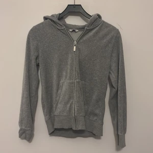 Grå hoodie med dragkedja och huva - En basic grå hoodie med dragkedja framtill och stor huva. Tröjan har långa ärmar, ribbade muddar och en praktisk ficka på magen. Perfekt för chill dagar eller när du vill ha något bekvämt och enkelt.