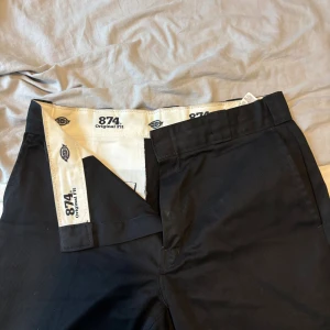 Svarta Dickies 874 byxor - Klassiska svarta Dickies 874 Original Fit byxor med raka ben och normal passform. Byxorna har diskreta bakfickor och Dickies-logga ovanför ena fickan. Tillverkade i slitstarkt material som ger en clean och tidlös look.