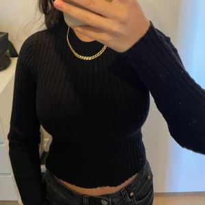 Svart ribbad croppad tröja - Snygg svart croppad tröja med ribbad struktur och lång ärm. Tröjan har en tight passform och rund halsringning, perfekt att matcha med höga jeans. Enkel och stilren design som passar dig som gillar minimalistiskt mode.