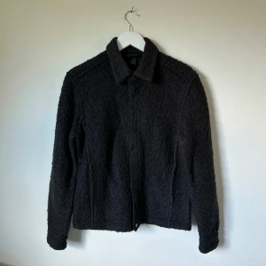 Svart H&M teddyjacka med krage - Mysig svart jacka från H&M med klassisk krage och knäppning framtill. Jackan har en fluffig och strukturerad yta, raka ärmar och diskreta fickor i sidorna. Perfekt för dig som gillar en stilren look med extra komfort. 3Å14