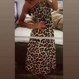 Leopardmönstrad långklänning - Säljer en snygg långklänning med leopardmönster och smockad överdel. Klänningen har tunna axelband och en loose passform som ger en avslappnad vibe. Perfekt för dig som vill sticka ut med ett djurmönster. Färgerna går i beige, svart och brunt.