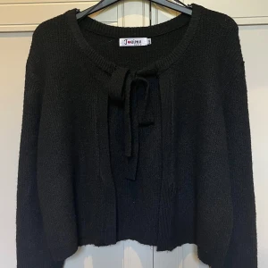Svart stickad kofta med knyt från J'aime - Svart stickad kofta från Missäy (J’aime OLYTO) i storlek M/L. Koftan har rund halsringning och snyggt knyt framtill. Långärmad och mjuk, perfekt för lager-på-lager. Koftan är köpt på Missäy men märket är J’aime OLYTO. 