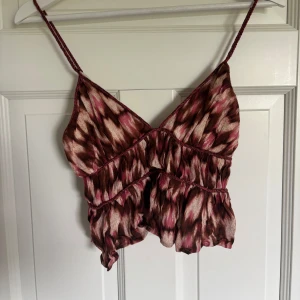 Mönstrad linnetopp från H&M XS - Säljer en snygg linnetopp från H&M i storlek XS. Toppen har ett brunt, rosa och beige mönster med volangdetaljer och smala axelband. Perfekt för varma dagar och ger en cool, avslappnad vibe. Aldrig använd.