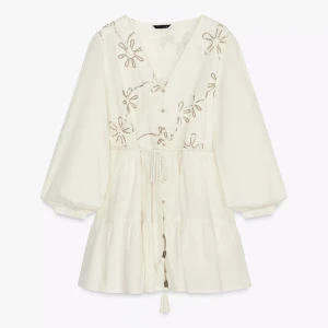 Vit kortklänning med broderade blommor - Superfin vit kortklänning med v-ringning, broderade blommor och knyt i midjan. Klänningen har vida ärmar och volang nedtill. Aldrig använd med lappen kvar!🥰