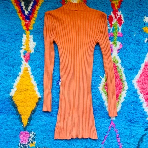 Ribbad orange långärmad klänning - Säljer en ribbad orange klänning med lång ärm och hög hals. Klänningen är kort och har en snygg figurnära passform som framhäver siluetten. Perfekt för dig som gillar färg och vill sticka ut lite extra.