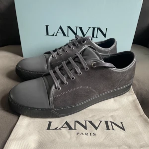Lanvin i mocka och skinn - Snygga grå sneakers från Lanvin med stilren design. Ovandel i mjuk mocka och tåparti i slätt skinn, matchande grå snörning och platt svart sula. Perfekta för dig som gillar minimalistisk och lyxig stil. Kommer med originalkartong och dustbag.💯✅