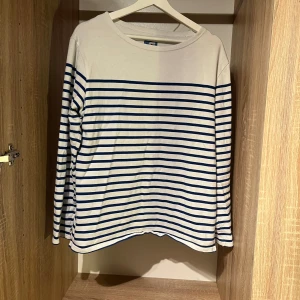 Randig långärmad tröja Mousqueton - Vit och marinblå långärmad tröja från klassiska franska märket Mousqueton med randigt mönster. Tröjan har rund halsringning och är tillverkad i mjuk bomull. 