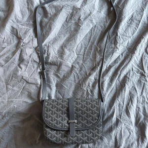 axelväska med mönster - Snygg axelväska i svart och grått med klassiskt grafiskt mönster. Väskan har justerbar axelrem, lock med spänne och detaljer i skinn. Perfekt storlek för det viktigaste och en ikonisk accessoar för dig som gillar lyxiga detaljer.