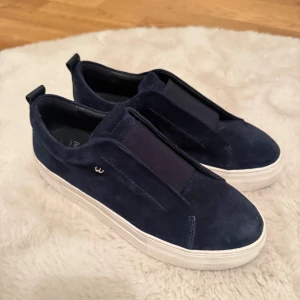 Mörkblå sneakers från W.Cobler - - Snygga mörkblå sneakers från W.Cobler i mocka med vit platt sula. Skorna har elastiskt band över vristen istället för snörning. Perfekta för dig som gillar stilrena och bekväma skor med modern touch. Typ använda 2-3 gånger då de känns för stora o kan ej lämna tillbaka tyvärr 