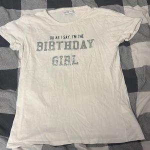 Vit t-shirt WOW Birthday Girl glitter - Vit t-shirt från WOW i storlek M-L med texten 'Do as I say, I'm the Birthday Girl' i glittriga silverbokstäver. Klassisk rund halsringning och korta ärmar. Perfekt för födelsedagsfirande och att sticka ut med ett statement.