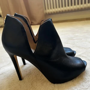 Svarta stövletter med öppen tå, strl 38 - Snygga svarta stövletter i skinn med hög klack och öppen tå. Skorna har en cool V-formad öppning vid ankeln och stilren design som ger en edgy vibe.