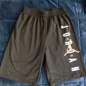 Svarta shorts från Nike (Air Jordan) - Svarta basketshorts från Nike med elastisk midja. Air Jordan logo i vitt och rött. Perfekta för en avslappnad stil eller sportiga aktiviteter.