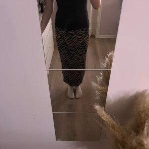 Zebramönstrad långkjol i beige och svart - Säljer en snygg långkjol med zebramönster i beige och svart. Kjolen har rak passform och sitter skönt i midjan. Perfekt för dig som vill sticka ut med ett djurmönster och gillar trendiga plagg.