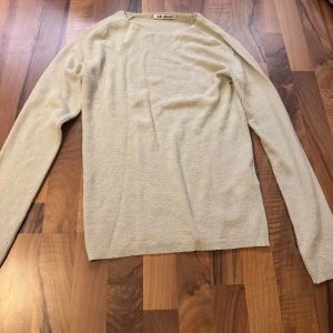 Beige stickad tröja från Our Legacy - Säljer en stilren beige stickad tröja från Our Legacy. Tröjan har en enkel design med rund halsringning och långa ärmar. Perfekt för lager-på-lager och funkar året runt. Materialet är mjukt och ger en avslappnad vibe.