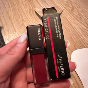 Shiseido LacquerInk LipShine röd - Snyggt rött läppglans från Shiseido, LacquerInk LipShine. Kommer i en stilren fyrkantig plastförpackning med svart lock och tydlig logga. Ger intensiv färg och glans till läpparna. Perfekt för dig som vill ha en djup röd nyans.