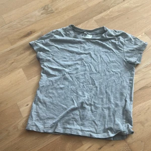 Grå basic t-shirt från Divided - Enkel grå t-shirt från Divided i storlek XXS. Klassisk modell med rund halsringning och korta ärmar. Tillverkad i mjuk bomull, perfekt för en clean och avslappnad stil.
