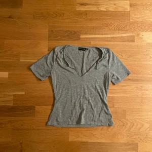 Grå v-ringad topp  - En enkel och stilren grå topp med v-ringning och korta ärmar. Toppen är i mjuk bomull och har en slim passform som sitter snyggt på kroppen. Perfekt att matcha med jeans eller kjol för en clean look.