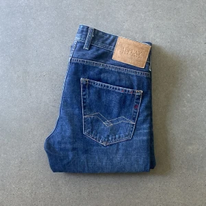 Blå Replay jeans, midwaist, straight fit - Säljer ett par klassiska blå jeans från Replay med raka ben och snygga slitningar. Jeansen har fem fickor, normal midja och tydliga sömmar på bakfickorna. Materialet är slitstarkt denim i bomull. Perfekta för en avslappnad och stilren look.